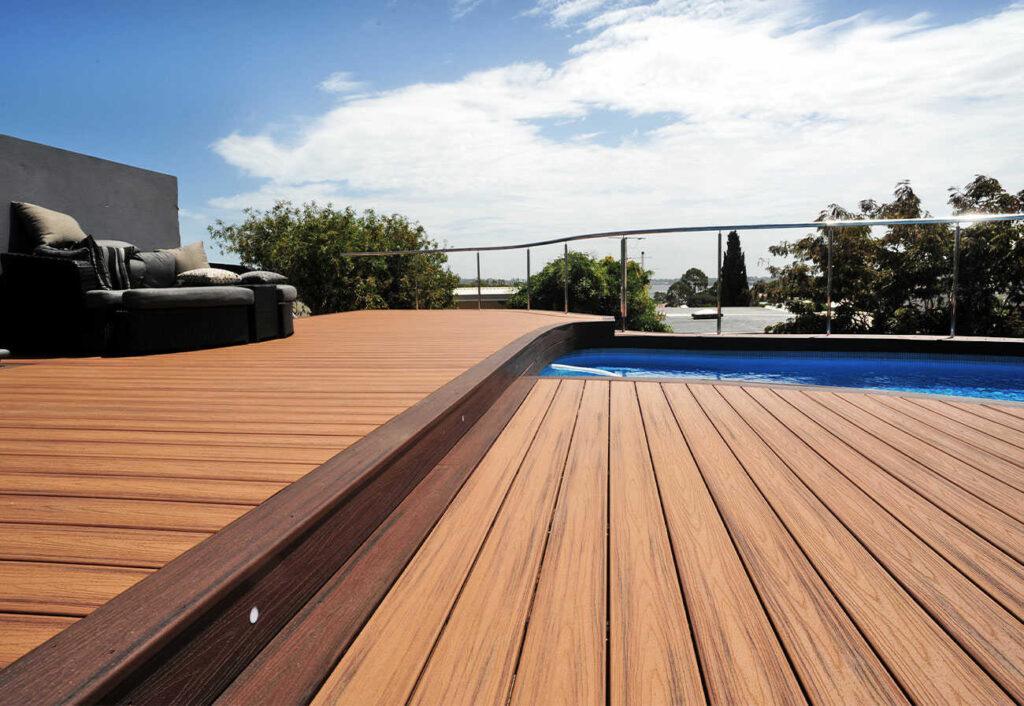 A wooden deck being cleaned with a brush near a glass railing.