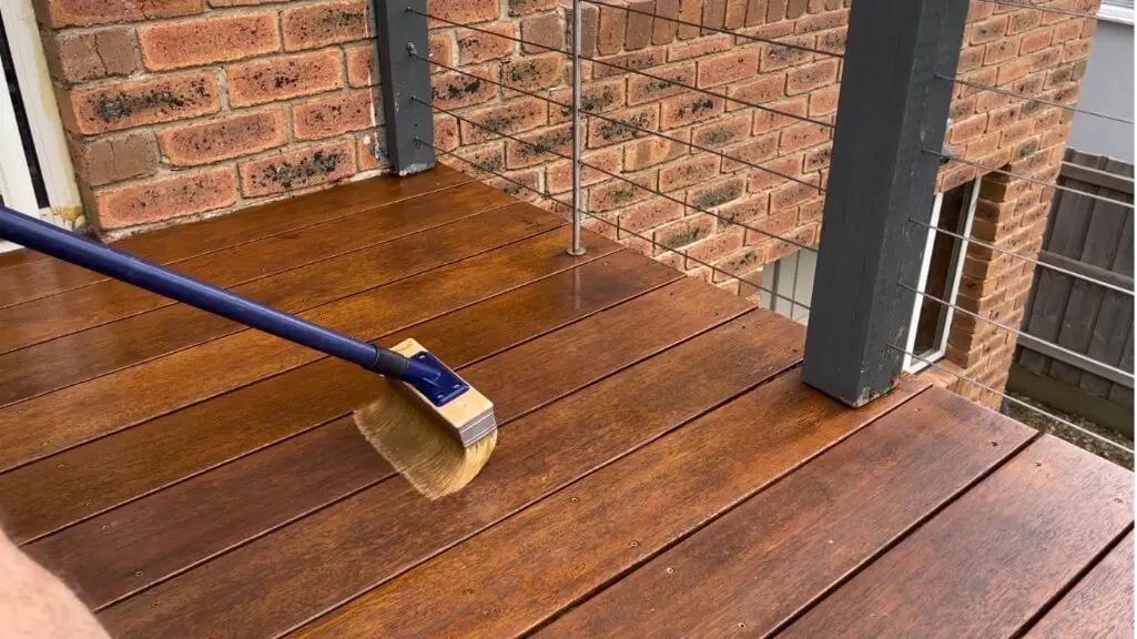 A wooden deck being cleaned with a brush near a glass railing.