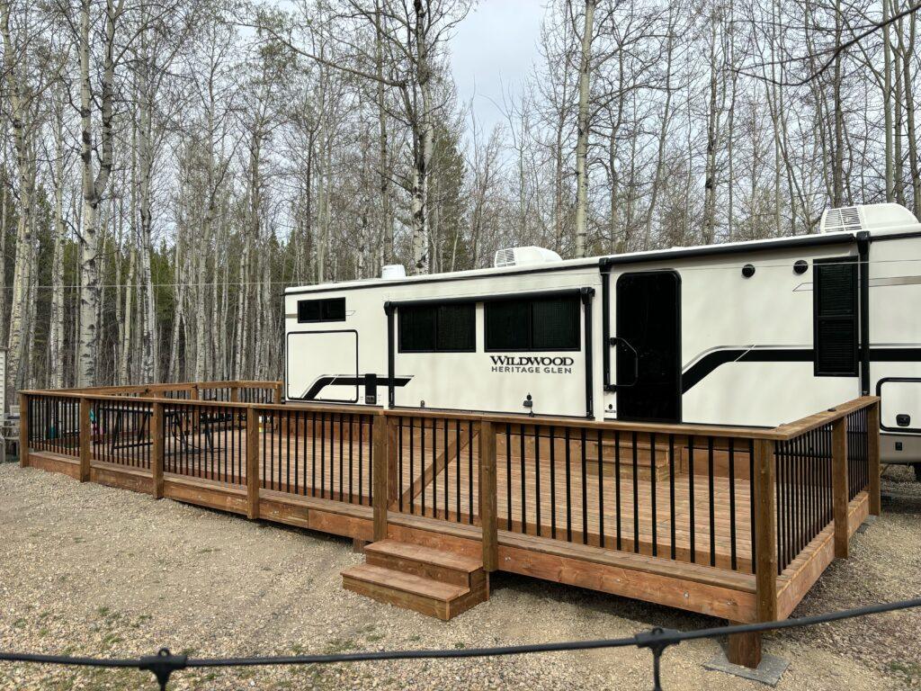 A large RV parked next to a wooden deck surrounded by trees.