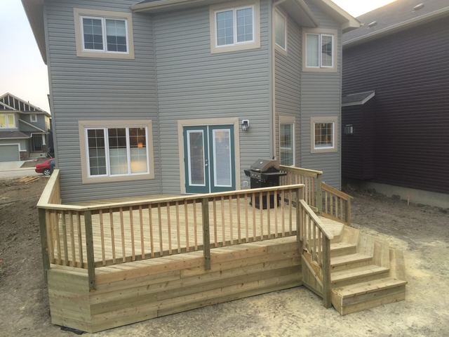 Wooden deck with railing and stairs attached to a gray house.
