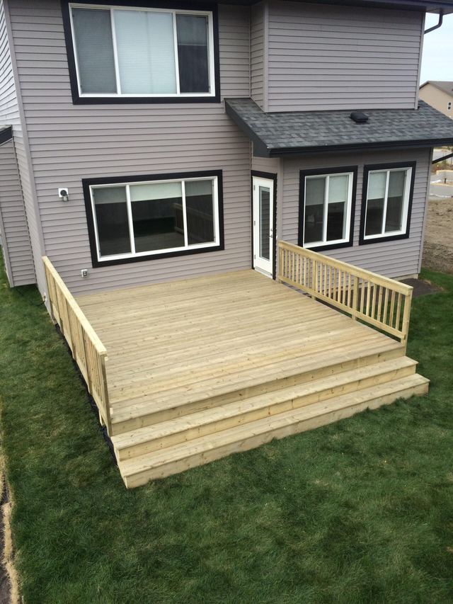 Newly built wooden deck with stairs and railing in backyard.