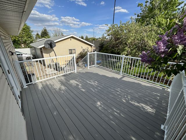 Spacious gray deck with white railing and garden view under a blue sky.