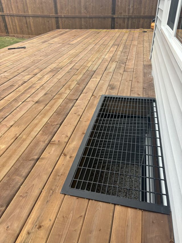 Wooden deck with a metal grate over a basement window well.