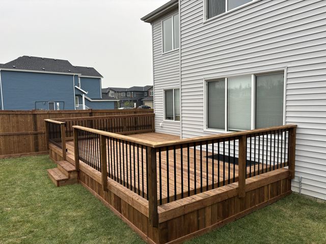 A large wooden deck attached to a house with railing and stairs.