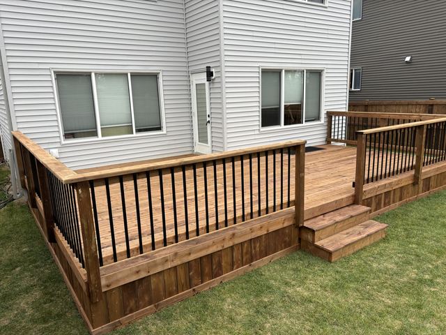 A small wooden deck with railing and stairs attached to a gray house.
