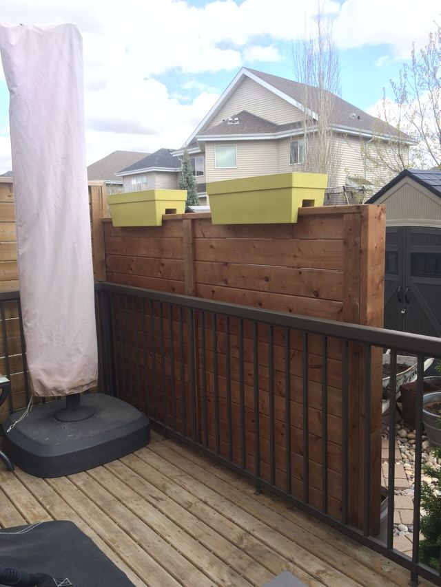 Two beehives placed on a wooden balcony railing with houses in the background.