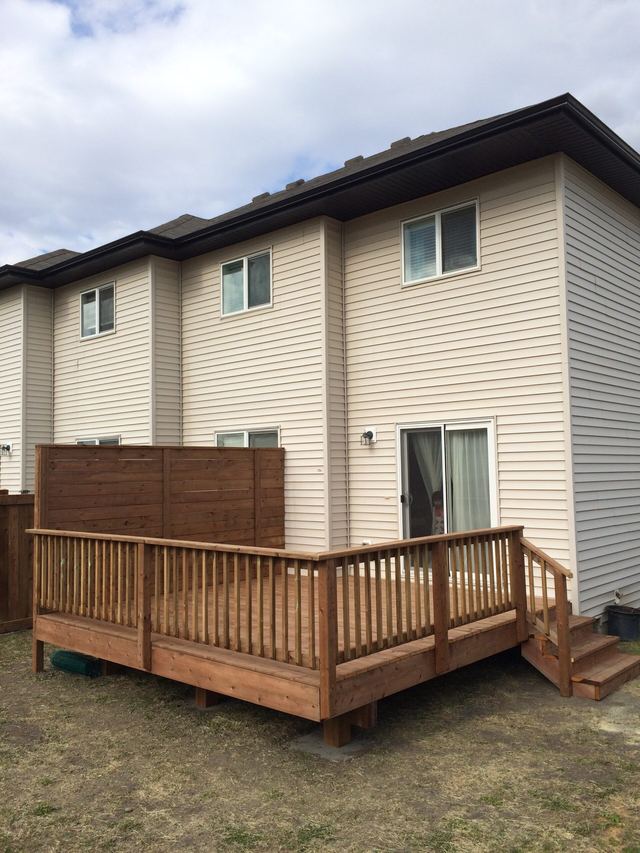 Wooden deck attached to a beige two-story house under a cloudy sky.