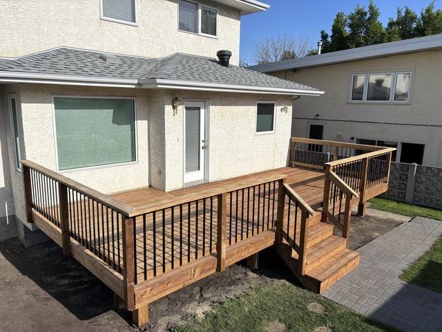 New wooden deck with black railings attached to a white house.