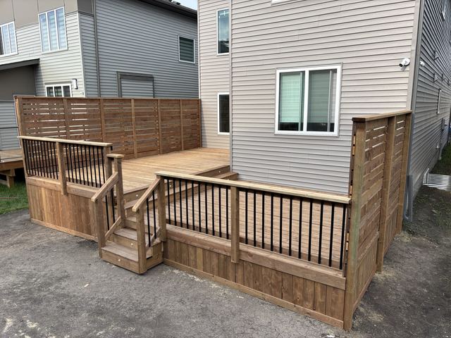 Wooden deck with stairs and railing adjacent to a house.