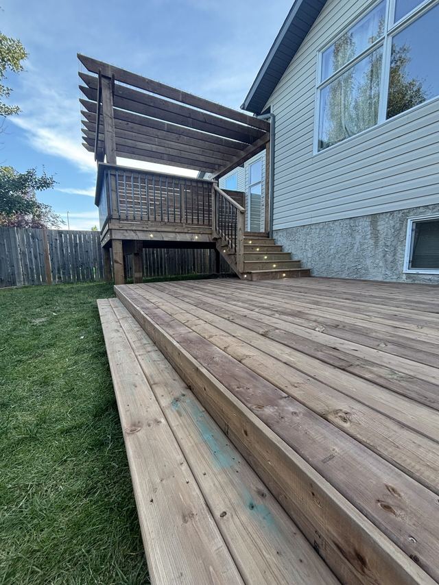 Wooden deck with a pergola and grill in a backyard.