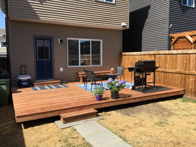 A wooden deck with outdoor furniture and a grill in a backyard.