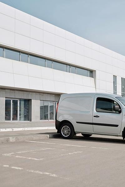 A white cargo van parked outside a modern industrial building.
