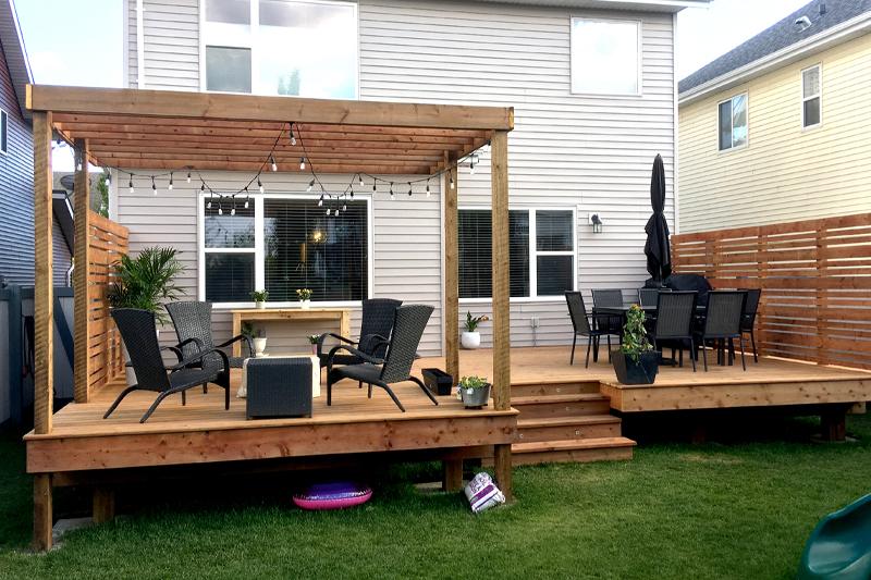 Modern backyard deck with seating and pergola attached to a house.