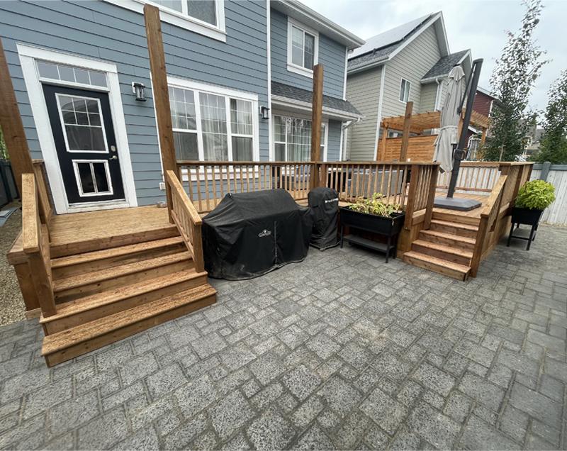 A cozy backyard patio with wooden stairs and a grill setup.