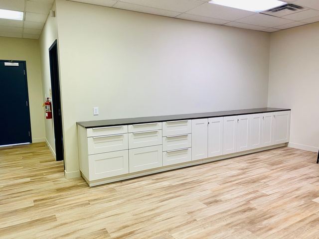 Long white cabinets with drawers in a room with light wood flooring.