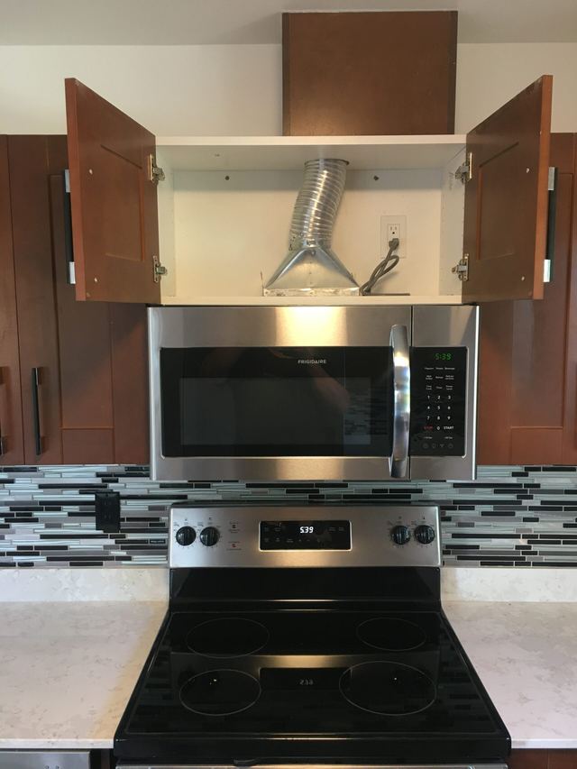 Modern kitchen setup with microwave and stove beneath open cabinets.