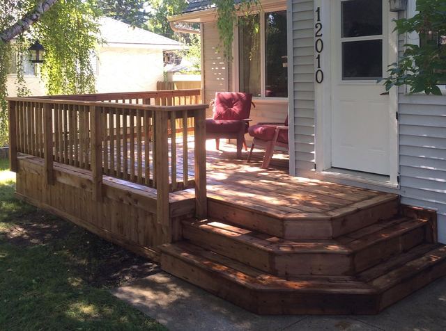 Wooden porch with steps and two red chairs in front of a house.