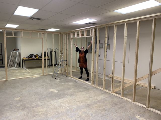 Person working on framing a wall inside a basement under renovation.