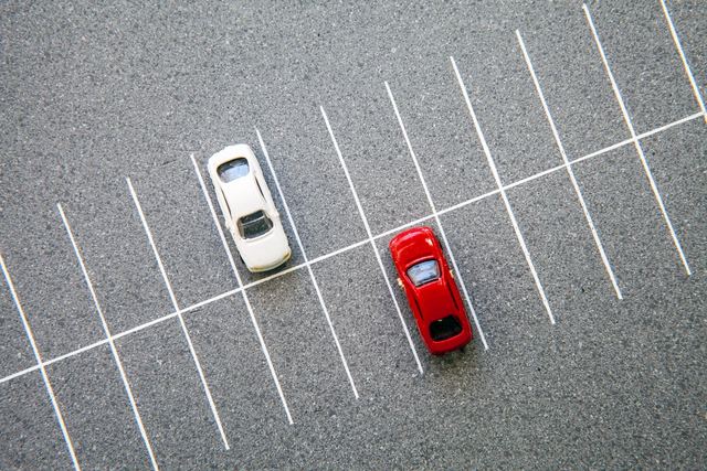 A white car and a red car parked in adjacent spaces in an empty lot.