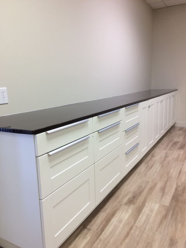 Long white kitchen cabinets with a black countertop and wooden floor.