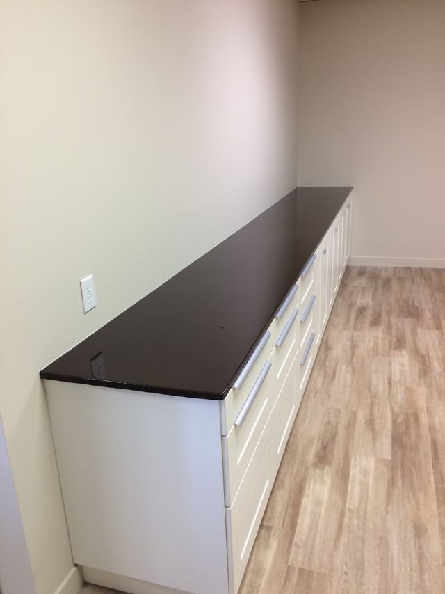 Long black countertop on white cabinets in a room with wooden flooring.