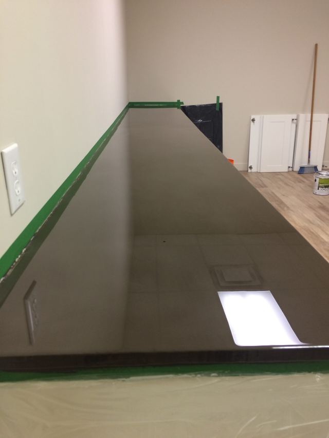 A long, reflective pool table with a green edge in a room.