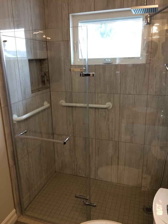 Modern glass shower with beige tiles and safety grab bars.