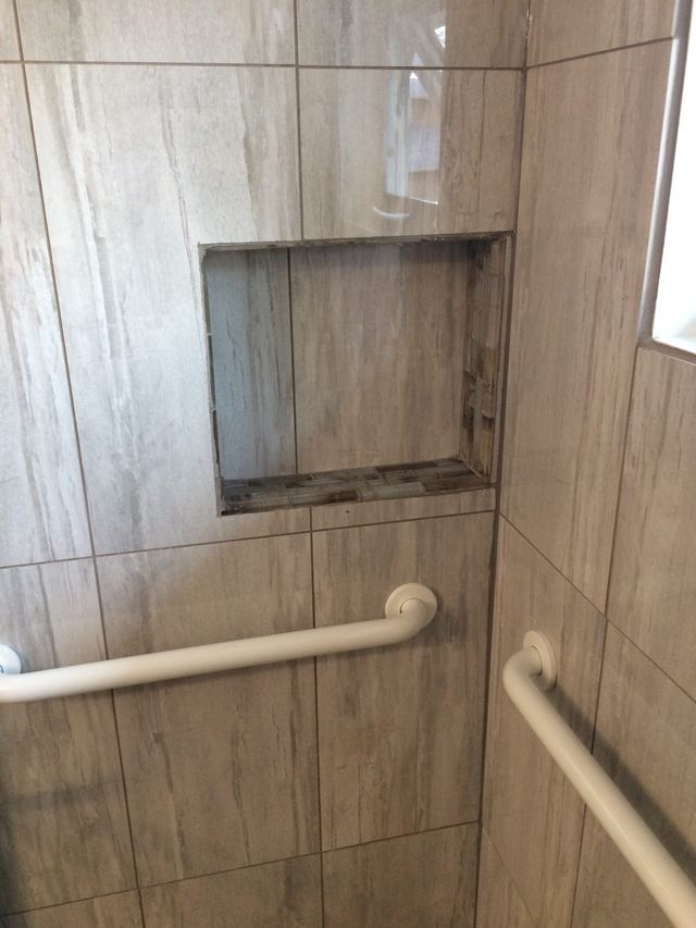 Empty recessed shower niche with grab bars in a tiled shower.