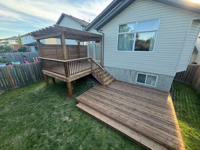 Wooden deck and gazebo attached to a house with green lawn.