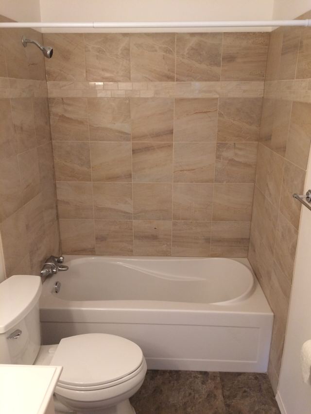 Small bathroom with bathtub and toilet in beige tiles.