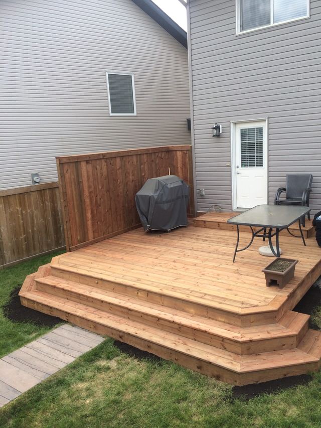 Multi-tiered wooden deck with a grill and outdoor seating in a backyard.