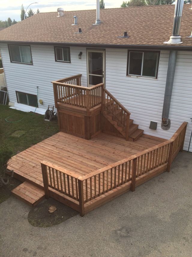 Newly built wooden deck and stairs attached to a white house.