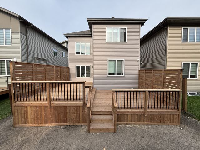 Back view of a two-story house with a wooden deck and stairs.