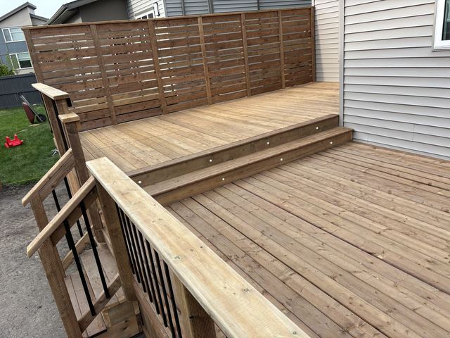 New wooden deck with steps and railing outside a house.