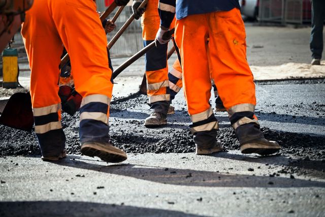 Workers in orange pants paving a road with asphalt.