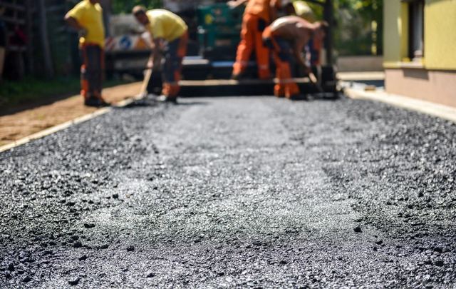Workers paving a fresh layer of asphalt on a road.
