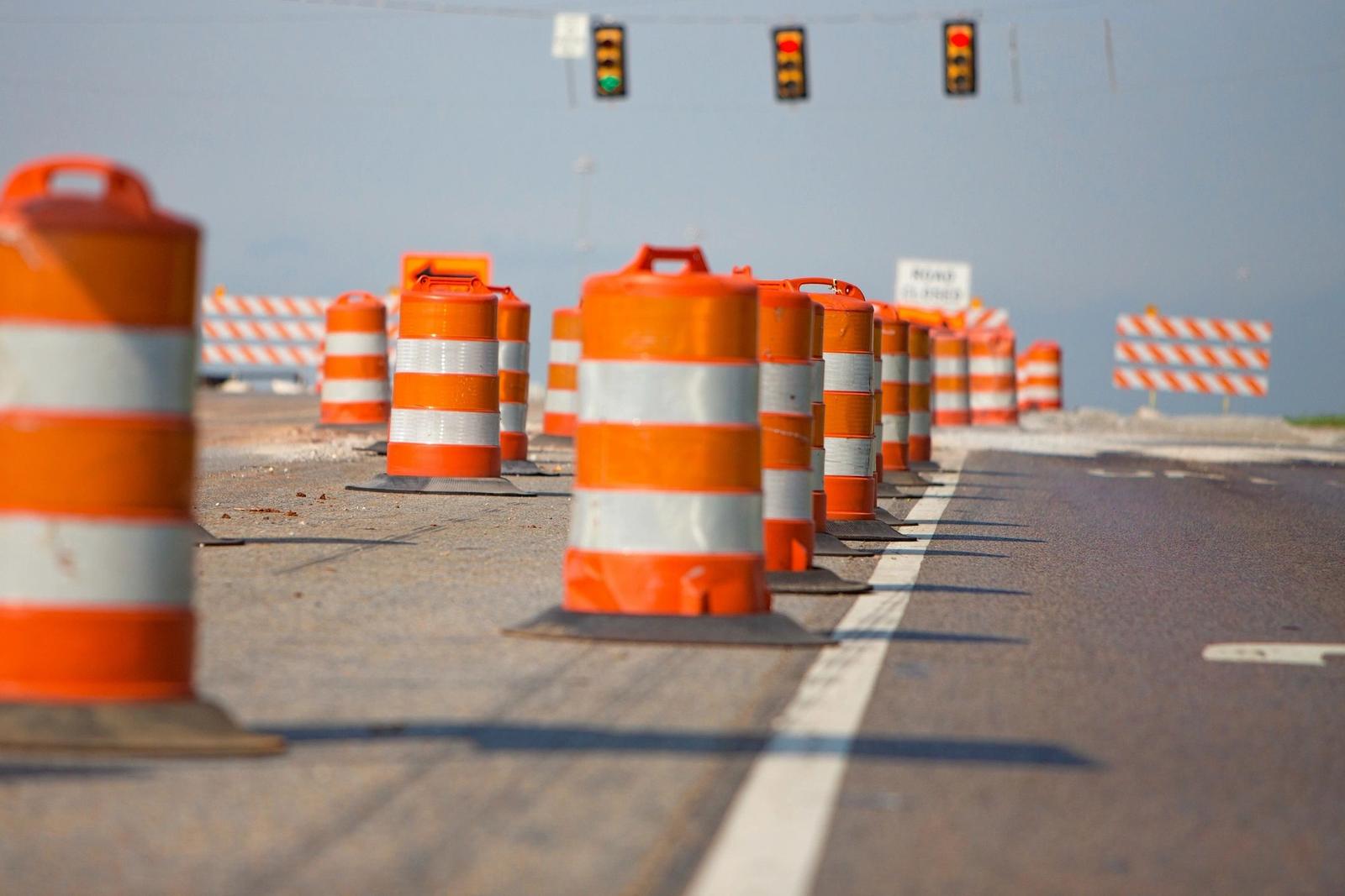 Orange and white traffic barrels line a road under traffic lights.