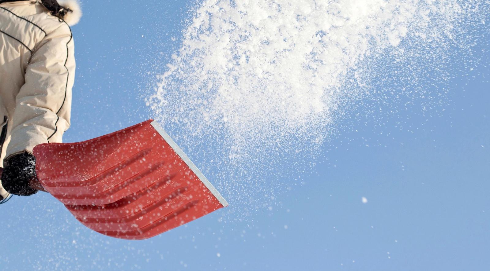 A red snow shovel throwing snow into the air against a blue sky.