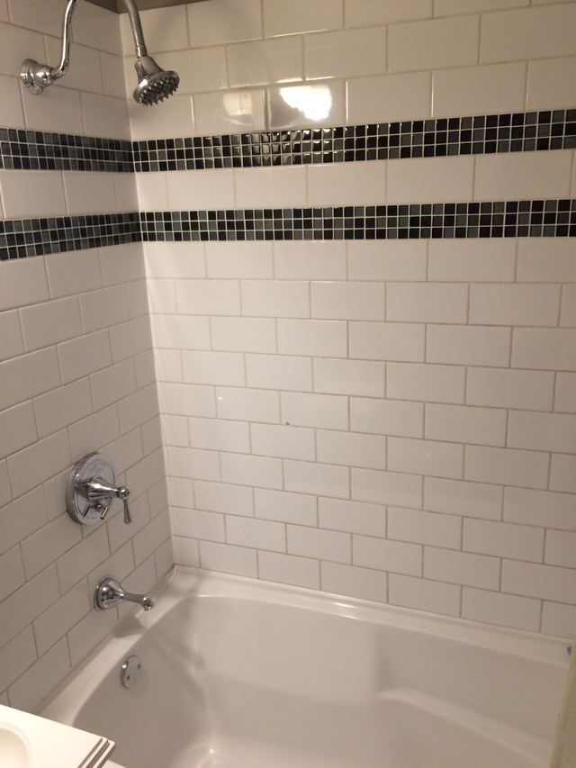 White subway tiles with black mosaic accent in a bathroom bathtub area.