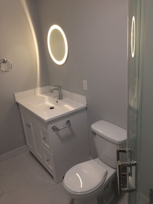 Minimalist bathroom with white sink, toilet, and illuminated mirror.