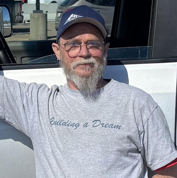 Older man with glasses and cap, smiling outdoors.