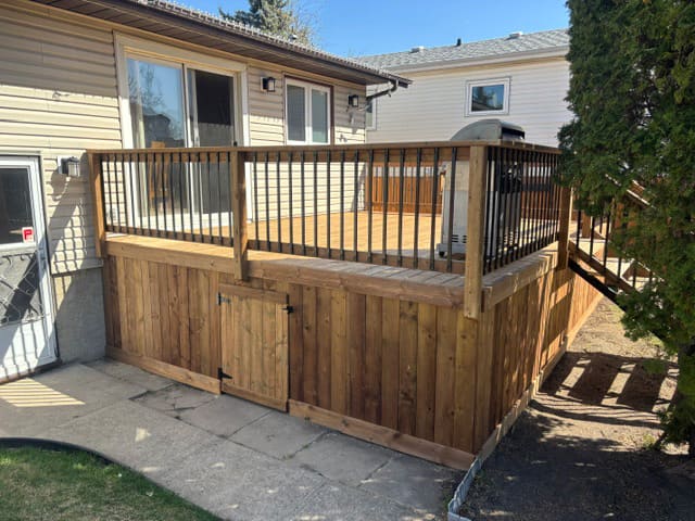 Newly built elevated wooden deck with black metal railings and secure gate in a residential backyard.